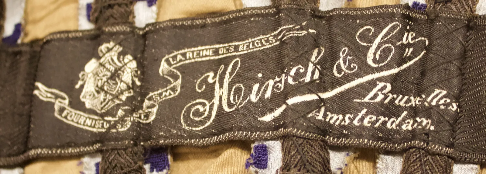 Label met tekst FOURNISEURS DE SM LA REINE DES BELGES / Hirsch & Cie / Bruxelles / Amsterdam