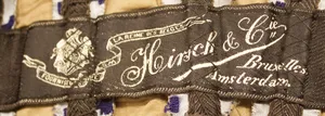 Label met tekst FOURNISEURS DE SM LA REINE DES BELGES / Hirsch & Cie / Bruxelles / Amsterdam