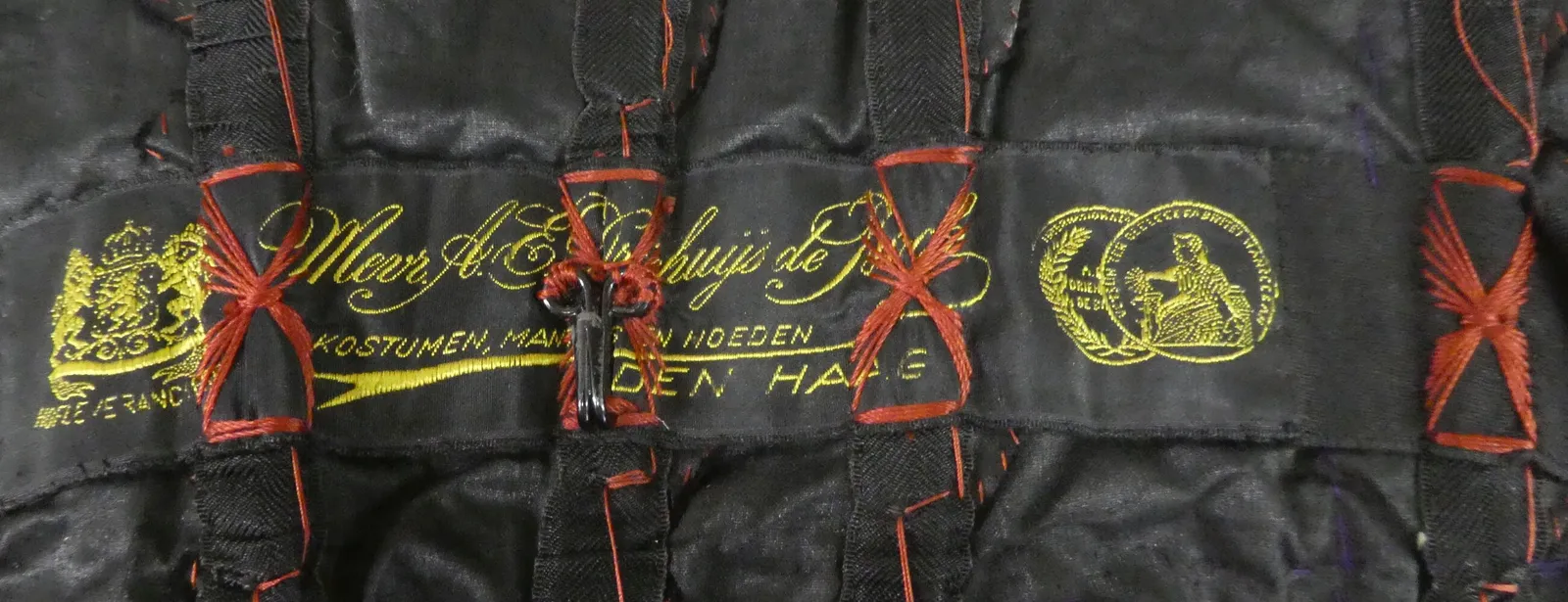 Label met tekst Mevr. A.E. Driehuijs de Bock / Kostumen, mantels en hoeden / Hofleverancier / Den Haag