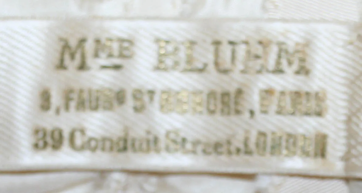 Label met tekst Mme. Bluhm / 3 Faubg St Honore, Paris / 39 Conduit Street, London