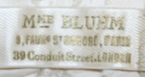 Label met tekst Mme. Bluhm / 3 Faubg St Honore, Paris / 39 Conduit Street, London