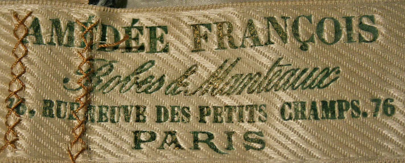 Label met tekst Amédée François / Robes & Manteaux / 76. Rue de Nve des Petits Champs, 76